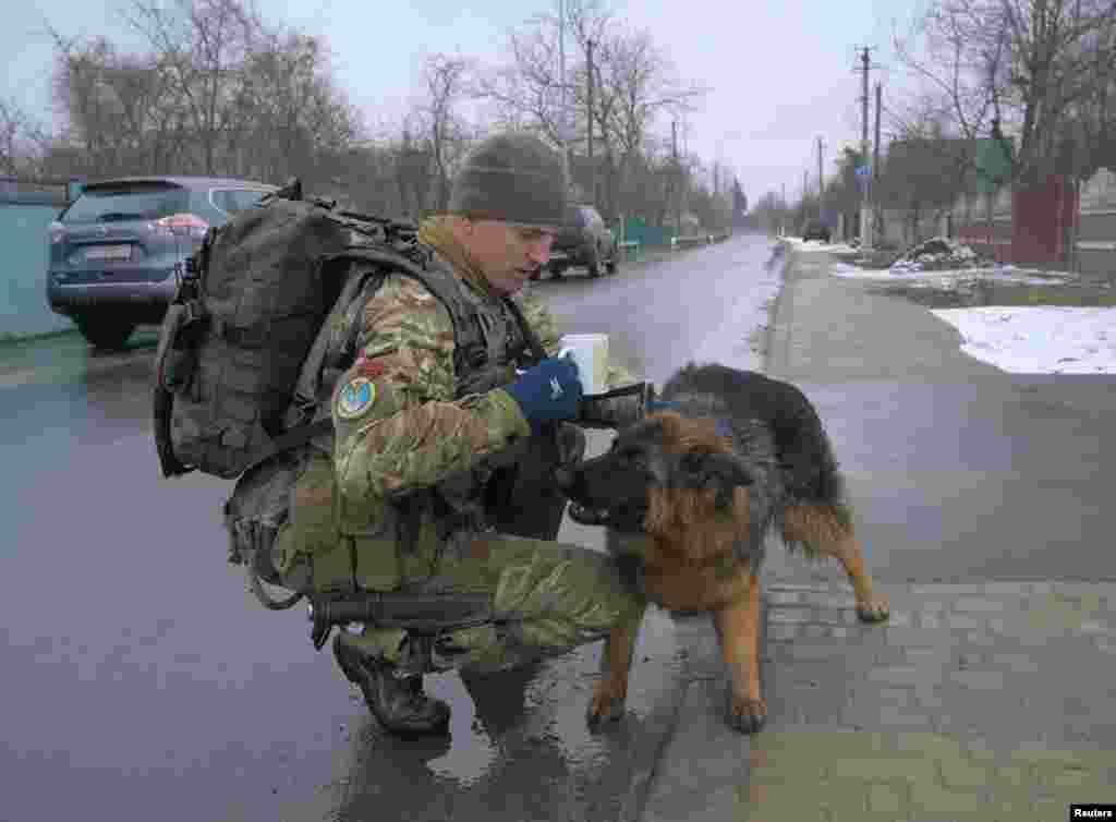 Український військовослужбовець гладить собаку на вулиці під час вторгнення Росії в Україну в селі Ясногородка Київської області, Україна, 2 березня 2022 року